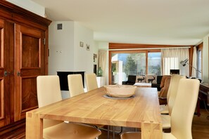 Ein Essbereich mit Holztisch und -stühlen, einer großen Schüssel in der Mitte und Blick ins Freie durch ein Fenster.