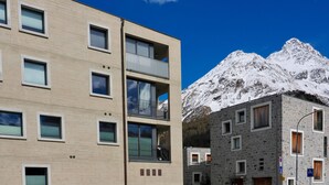 Un edificio moderno con varios balcones y montañas al fondo.