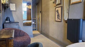 A hotel room with a bed, two armchairs, a small table, and a wall decorated with various framed items.