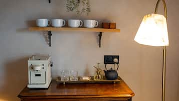 A kitchenette with a coffee maker, a tray with glasses, a teapot, and a shelf with cups.