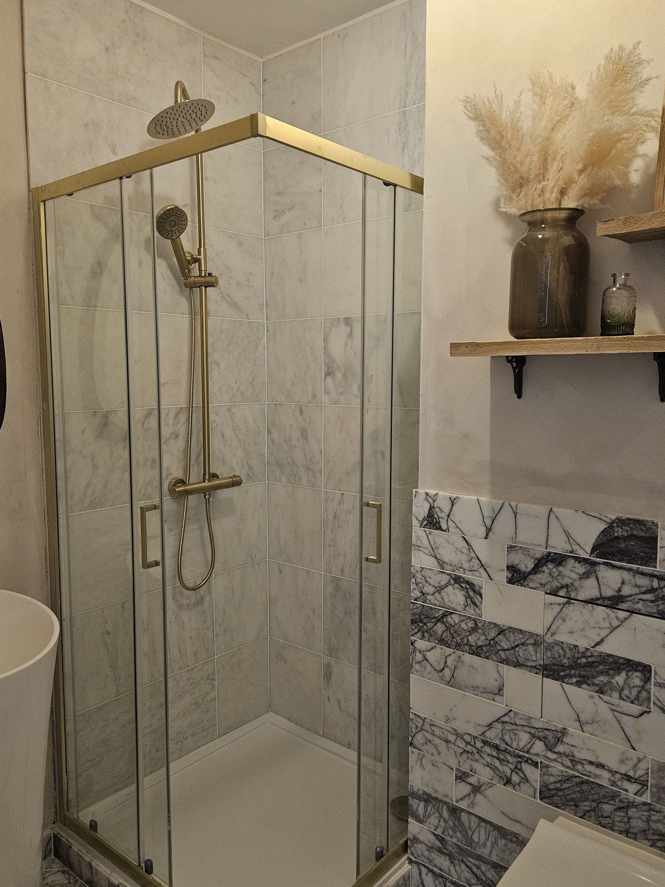 A glass-enclosed shower with a handheld showerhead and a handheld faucet.