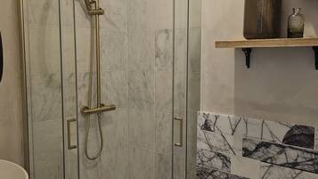 A glass-enclosed shower with a handheld showerhead and a handheld faucet.