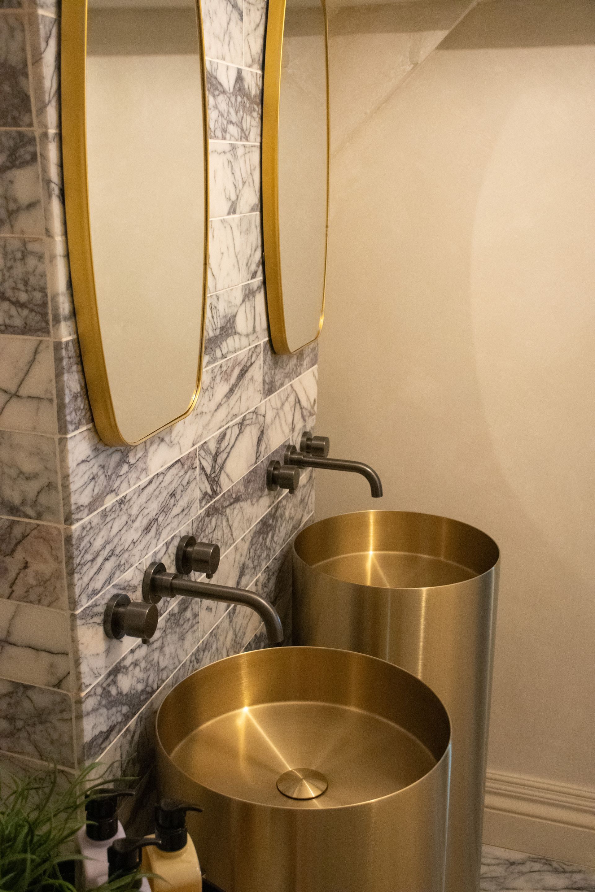 Een badkamer met marmeren wanden, een spiegel met gouden lijst en een gouden wastafel.