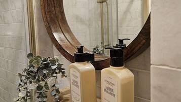 A bathroom with a wooden shelf holding two bottles of body lotion and a mirror with a wooden frame.