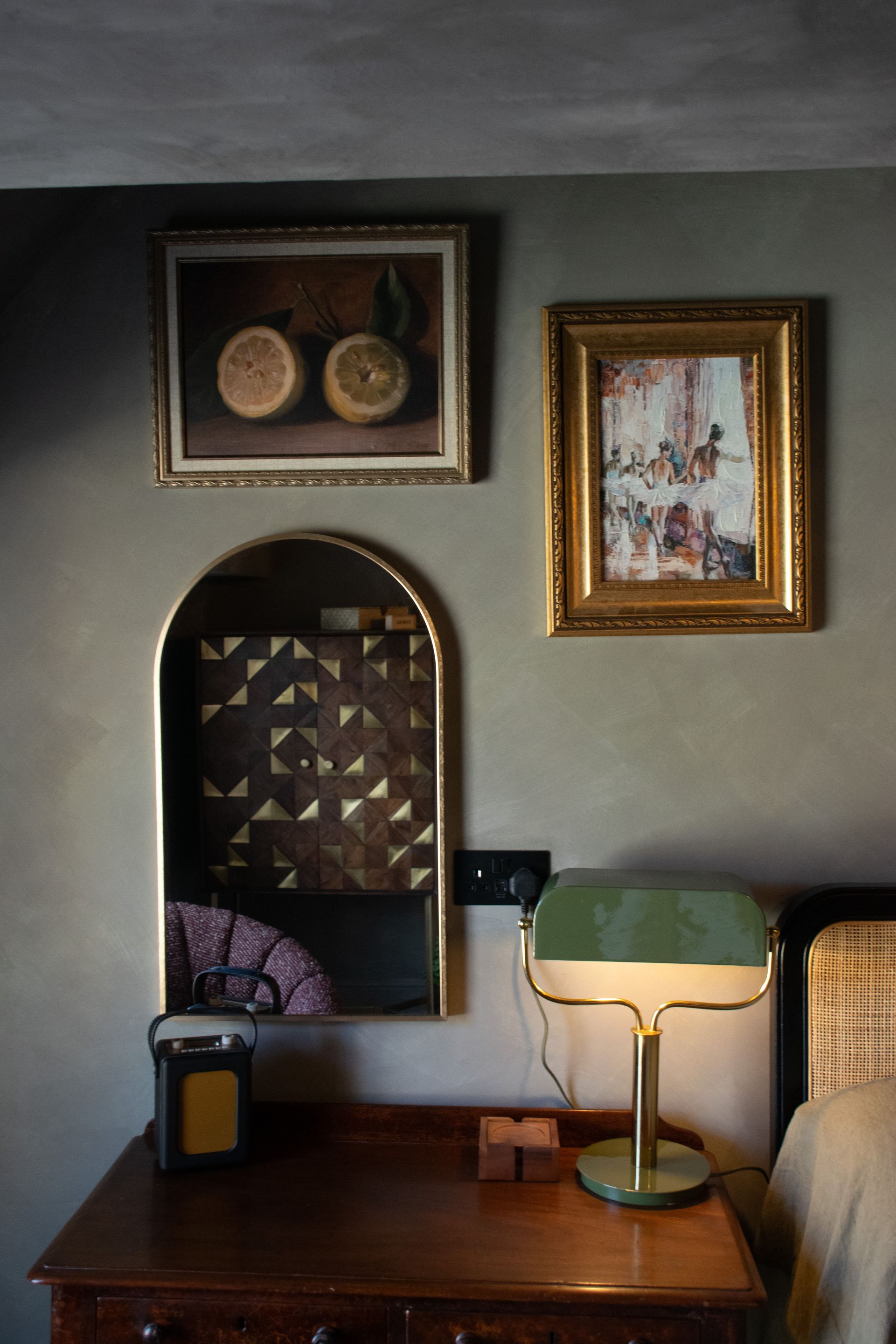 A room with a desk, a lamp, a mirror, and two framed artworks on the wall.