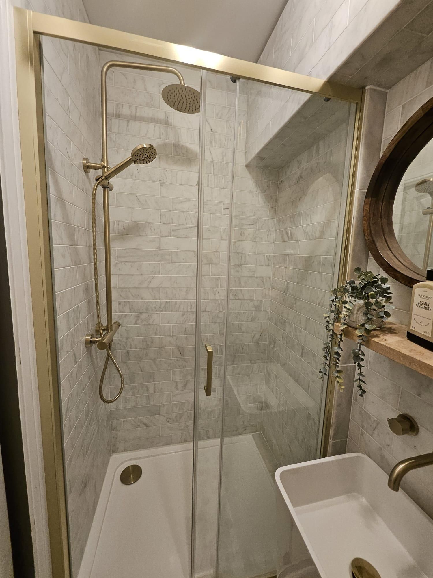 Una ducha a nivel con puerta de cristal, un lavabo blanco y un espejo sobre él.