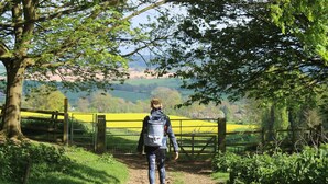 Una persona caminando por un sendero con vistas a un paisaje rural y una valla amarilla.