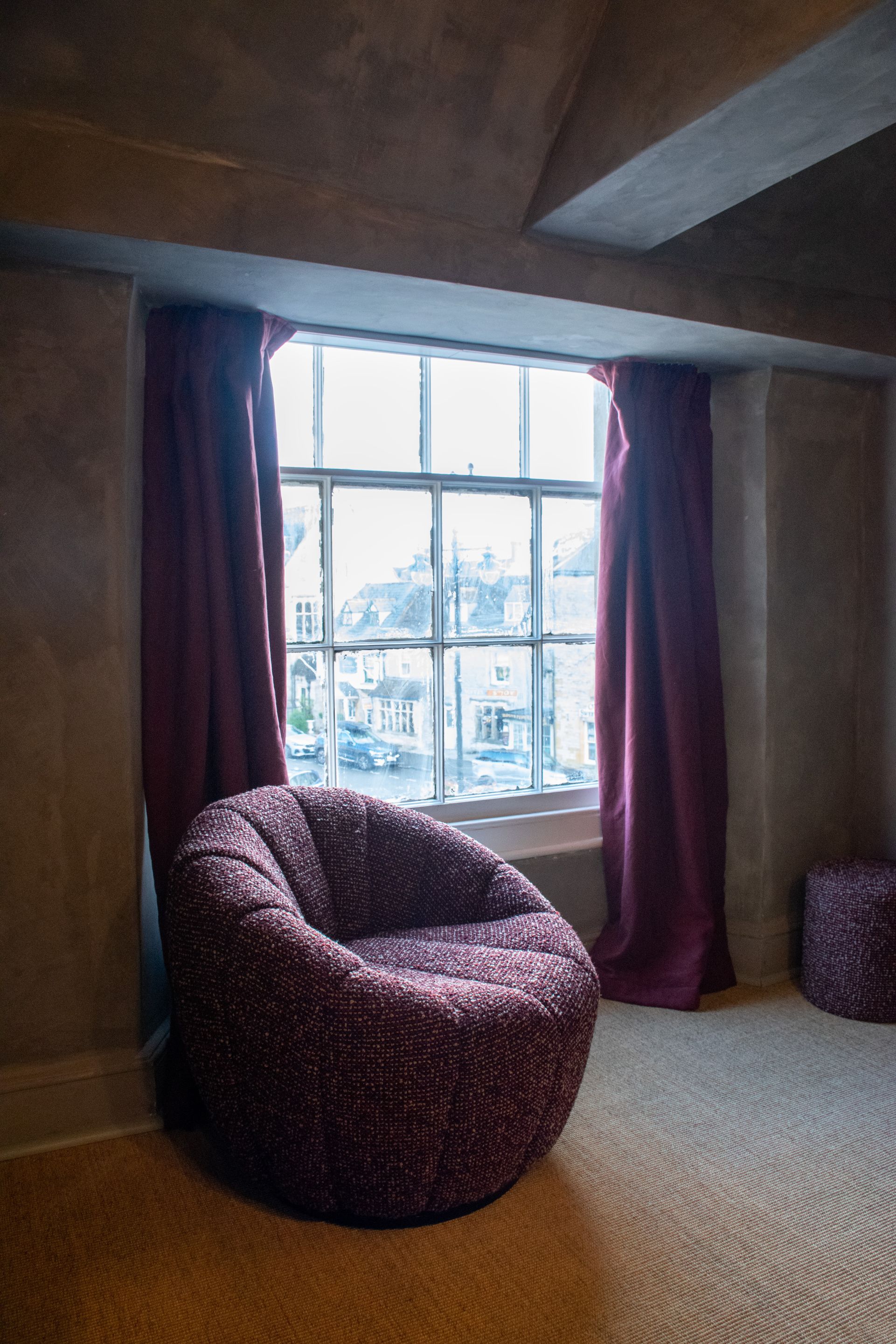 A room with a large window, a bean bag chair, and a small ottoman.