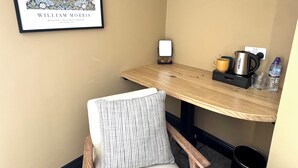 A corner room with a framed artwork, a table with a kettle, a cup, and a bottle, a chair, and a trash bin. - Charlie's Quarters Self Check-In Rooms (Brampton)
