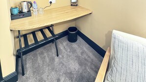 A small room with a wooden desk, a TV mounted on the wall, a coffee maker, a water bottle, and a trash can. - Charlie's Quarters Self Check-In Rooms (Brampton)
