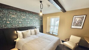 A bedroom with a large bed, a chair, a window with blinds, a wall-mounted light, and a framed picture. - Charlie's Quarters Self Check-In Rooms (Brampton)