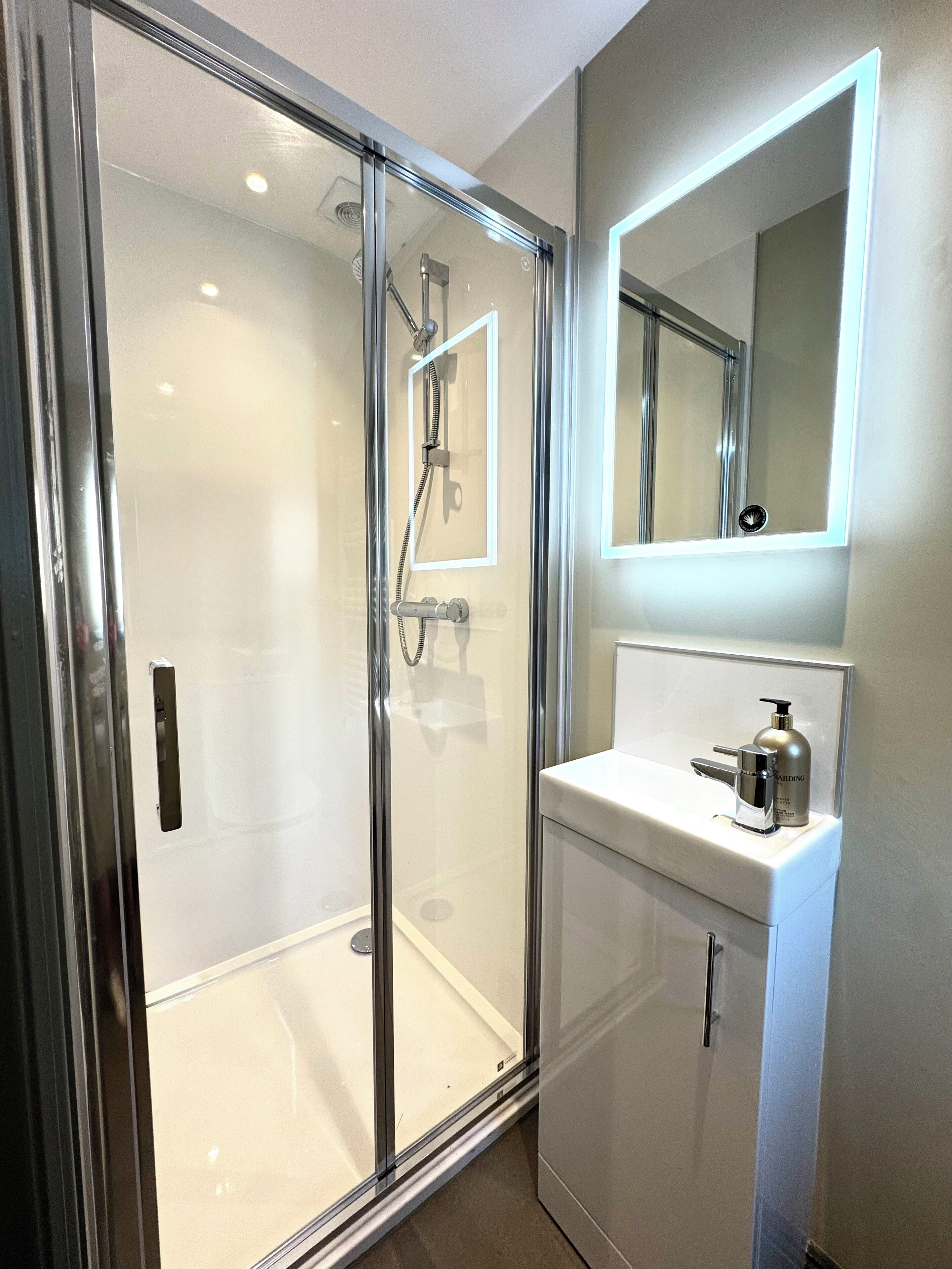 A modern bathroom with a glass-enclosed shower, a white sink, and a mirror above the sink.