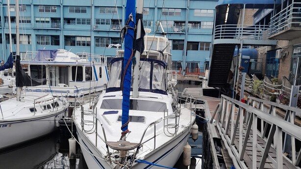 Um cais com vários barcos atracados, um edifício com janelas azuis ao fundo, e uma barreira de corda em primeiro plano.