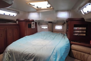 A compact RV interior with a bed, a small window, and a storage cabinet.