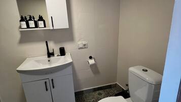 Un baño con lavamanos blanco, espejo, inodoro, baldosas de suelo estampadas y un armario blanco.