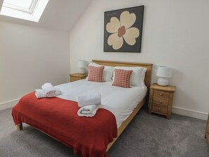 A neatly made bed with a red blanket, white pillows, and two bedside lamps. - Glynllifon 8 (Marianglas)