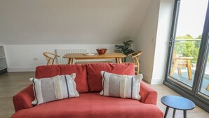 Ein rotes Sofa mit zwei Kissen, ein kleiner runder Tisch, ein Holzesstisch und Blick ins Grüne.