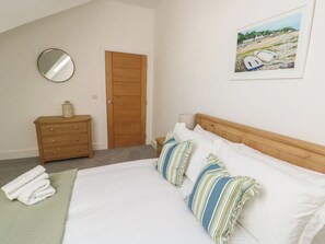 Ein Schlafzimmer mit einem Bett, Kissen, einem Schminktisch, einem Spiegel, einer Tür und einem Bild an der Wand.