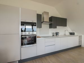 A modern kitchen with built-in appliances, a large window, and a view of the outdoors. - Glynllifon 8 (Marianglas)