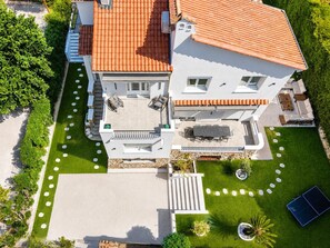 Ein modernes, zweistöckiges Haus mit einem Ziegeldach, einer Terrasse mit Gartenmöbeln und einem gepflegten Rasen.