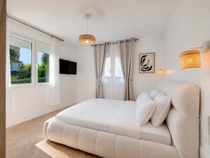 Ein Schlafzimmer mit Bett, Vorhängen, einem an der Wand befestigten Fernseher und einer Wandleuchte.