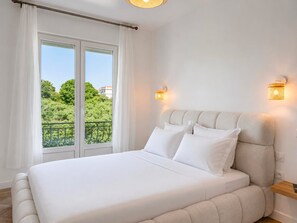 Ein Schlafzimmer mit einem großen Bett, weißen Vorhängen, einem Balkon mit Geländer und zwei Wandleuchten.