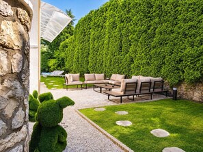 Eine Terrasse mit Gartenmöbeln, einer Steinmauer und einer gepflegten Hecke.