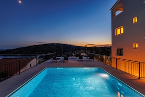 Ein Pool mit Blick auf eine Hügellandschaft, Sitzmöglichkeiten im Freien und ein Gebäude mit Fenstern.
