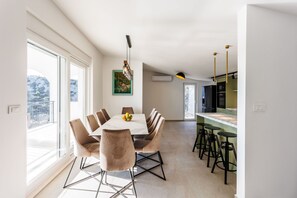 Ein moderner Essbereich mit einem großen Tisch, Stühlen und Blick durch große Fenster.