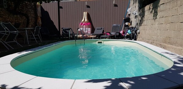 Una piscina de borde curvo, rodeada de sillones de descanso y una cerca de madera.