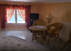 Una habitación con una cama, una mesa con papeles, una silla, un televisor y una ventana con cortinas.