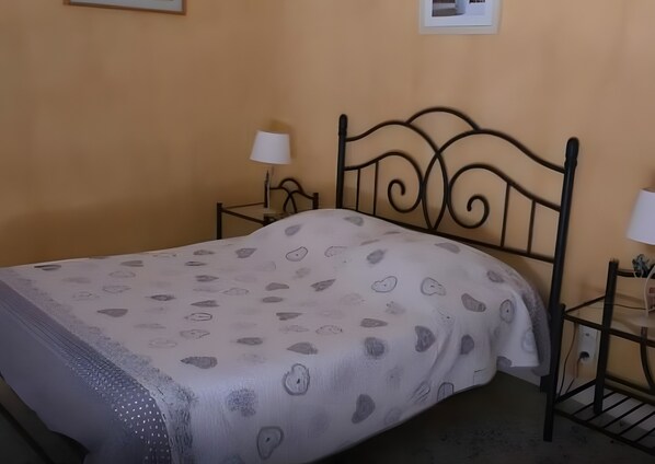 Una cama con una colcha estampada, dos mesitas de noche con lámparas y un cuadro colgado en la pared.
