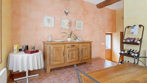 Une pièce avec une table en bois, une nappe blanche, un meuble en bois orné d’une plante et un porte-bouteilles.