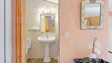 A bathroom with a pedestal sink, a mirror with a decorative frame, and a potted orchid on a table.