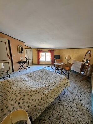 Un dormitorio con una cama, una silla, una mesa, un radiador y una ventana con cortinas.