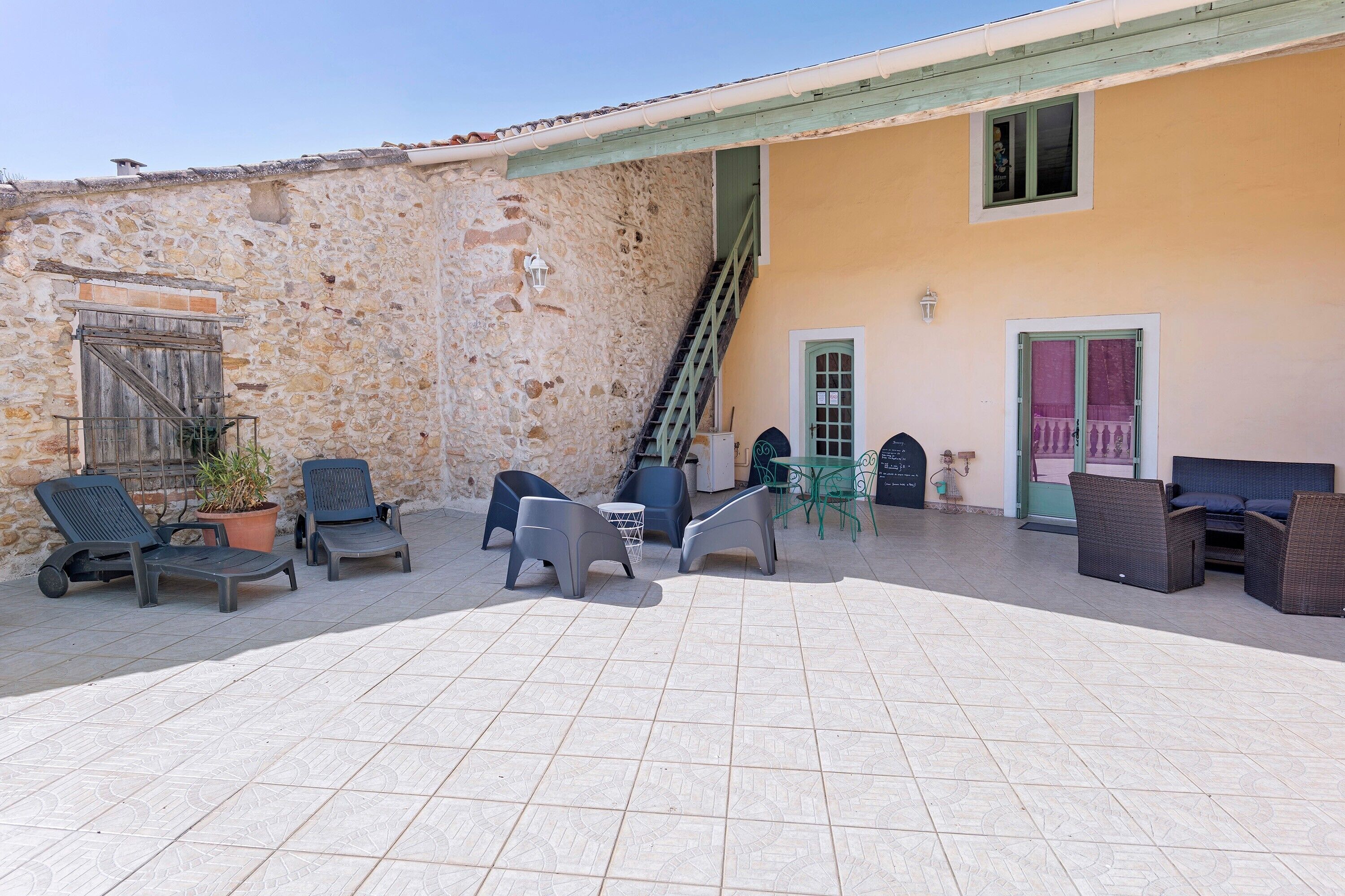 A courtyard with outdoor seating, a staircase, and a building with a stone wall and a yellow facade.