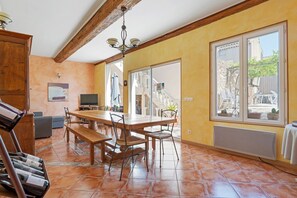 A dining area with a wooden table and chairs, a bench, a TV, and a large window with a view of the outside.