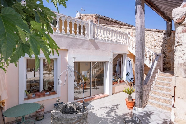 A courtyard with a stone table, potted plants, and a staircase leading to a balcony.