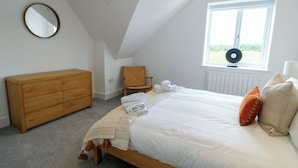 A bedroom with a bed, a wooden dresser, a chair, a window, and a radiator. - Glynllifon 9 (Marianglas)
