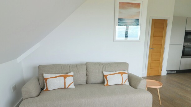 A living room with a sofa, two pillows, a small side table, and a framed picture on the wall. - Glynllifon 9 (Marianglas)