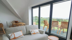 A modern living room with a sofa, a small round table, and a dining area with a table and chairs. - Glynllifon 9 (Marianglas)
