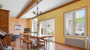 A dining area with a wooden table and chairs, a bench, a TV, and a large window with a view of the outside.