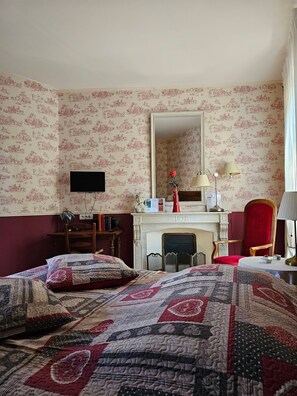 Una habitación de hotel con cama, escritorio, silla, chimenea y televisión.