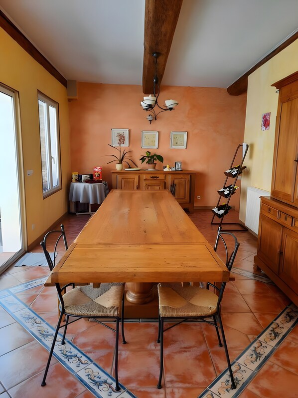 Un comedor con una larga mesa de madera, sillas, una lámpara de araña y piso de baldosas.
