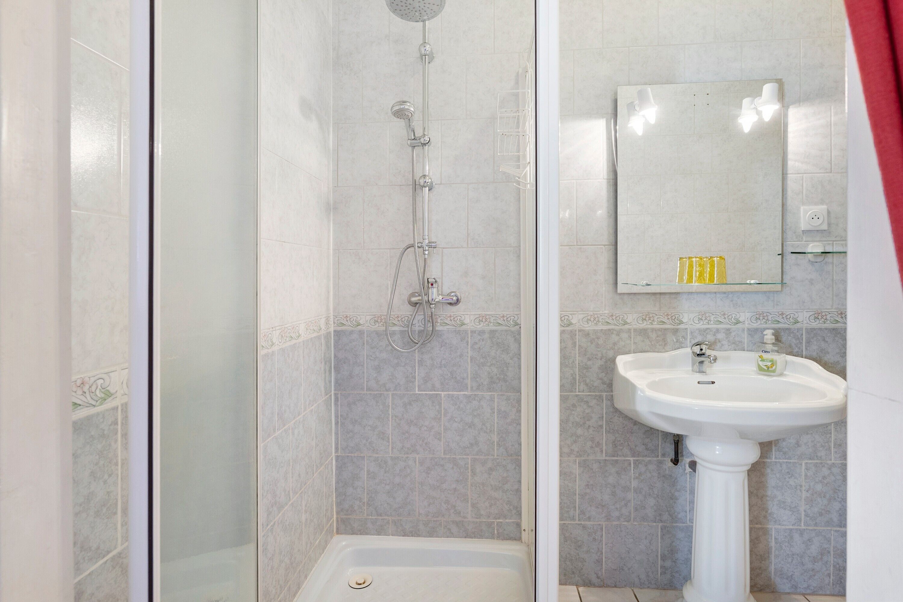 Un baño con cabina de ducha de vidrio, lavamanos pedestal y espejo sobre él.
