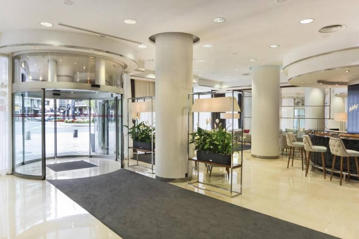 Eine moderne Hotelhalle mit einer Drehtür, einem Empfangstresen und einer Sitzecke mit Stühlen.