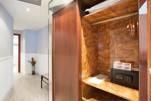 A room with a wooden wardrobe, a small desk with a telephone, and a plant.