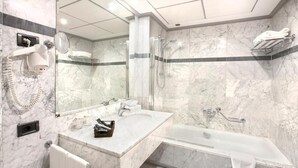 A modern bathroom with a marble wall, a large mirror, a hairdryer, a sink, a shower, and a bathtub. - Hotel Ini (Madrid)