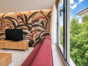 Ein modernes Wohnzimmer mit großem Fenster, einem Flachbildfernseher, einem Holztisch und einem roten Sofa.