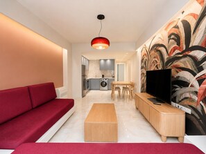 Ein modernes Wohnzimmer mit einem roten Sofa, einem Holztisch, einem Fernseher und einer Küche im Hintergrund.